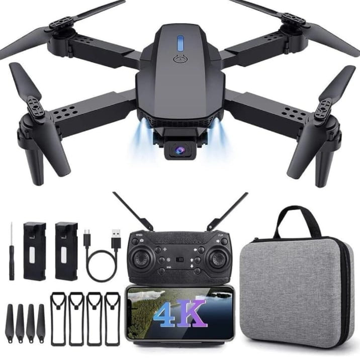 A foldable quadcopter drone with four black propellers, shown above its included accessories: a handheld remote controller, a smartphone with a 4K display, three battery packs, several screws, and a gray zippered carrying case on a plain white background.